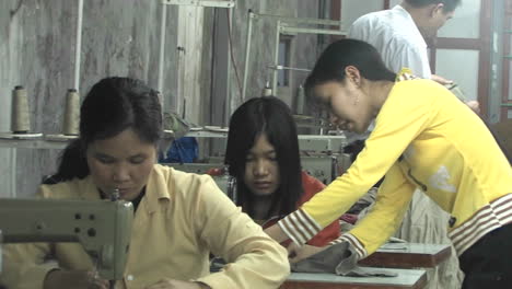 Una-Mujer-Asiática-Instruye-A-Una-Costurera-Que-Se-Sienta-En-Una-Máquina-De-Coser