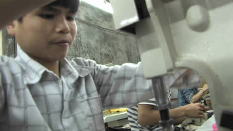 Ein-Kind,-Das-Versucht,-Mit-Hilfe-Eines-Mädchens-In-Einem-Sweatshop-In-China-Eine-Nähmaschine-Zu-Reparieren