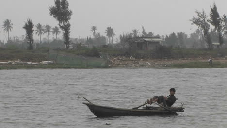 Ein-Kleiner-Junge-Segelt-Ein-Boot-In-Einem-Fluss,-Der-Mit-Seinen-Füßen-Auf-Dem-Mekong-In-Vietnam-Rudert