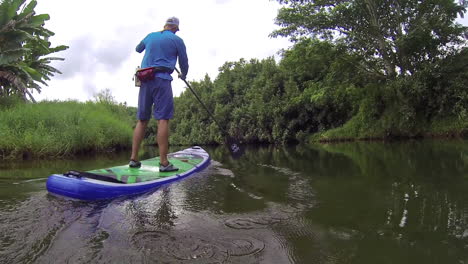 A-man-rows-a-paddleboard-down-a-river-in-Kauai-Hawaii-1