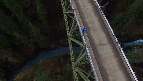 An-aerial-over-a-man-walking-on-a-steel-suspension-bridge-over-the-Skokomish-River-in-Washington-USA