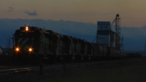 A-Freight-Train-Passes-A-Grain-Silo-At-Dusk