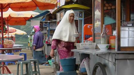 A-Woman-Wearing-A-Muslim-Dress-Carries-A-Plate-In-An-Outdoor-Eatery
