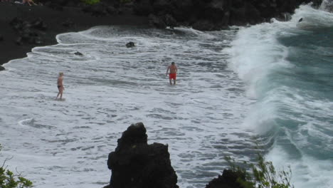 A-Man-Battles-Large-Waves-Along-A-Black-Sand-Beach-In-Hawaii