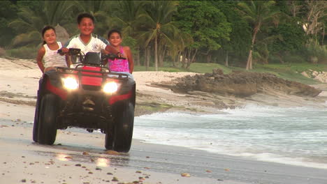 A-man-and-two-children-ride-an-ATV-through-the-water-on-a-beach