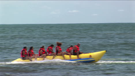A-group-of-young-people-wearing-red-life-jackets-ride-through-the-water-on-a-yellow-boat