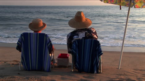 A-couple-relaxes-in-beach-chairs-under-an-umbrella-while-watching-the-ocean