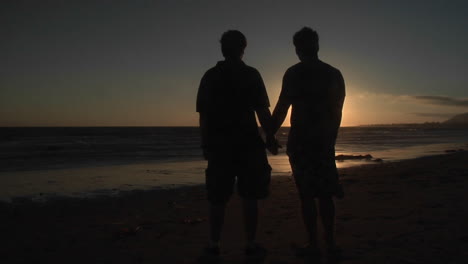 Silhouettes-of-two-men-hold-hands-on-a-windy-beach