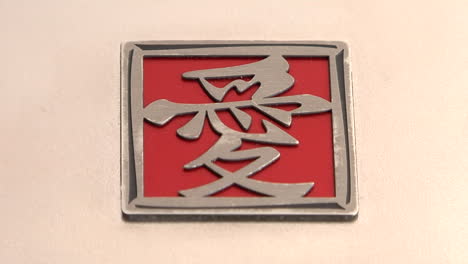 A-red-and-silver-square-with-Asian-characters-lies-on-a-pink-surface
