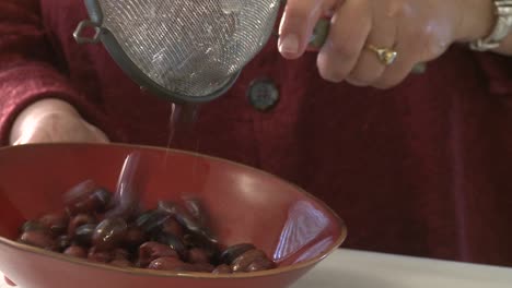 A-woman-pours-olives-from-a-strainer-into-a-bowl