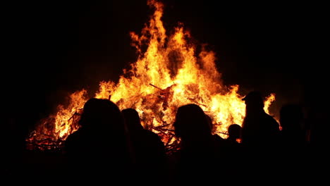 People-stand-in-front-of-a-large-raging-bonfire-at-night