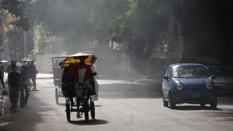 A-car-and-pedicab-drive-down-a-smoky-road-in-Havana-Cuba
