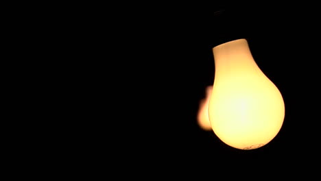 Three-bare-illuminated-light-bulbs-swing-against-a-black-background