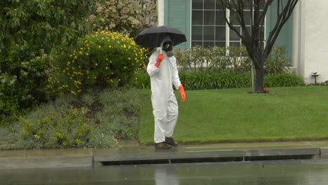 A-man-in-a-hazmat-suit-holds-an-umbrella-and-crosses-the-street