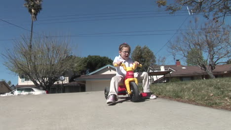 A-girl-loses-her-footing-on-a-plastic-tricycle-and-rolls-down-a-driveway