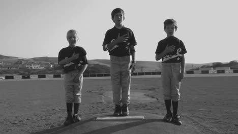 Black-and-white-shot-of-young-baseball-players-cover-their-hearts-with-their-hats