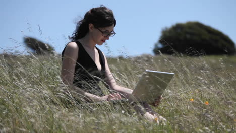 A-woman-sits-in-a-field-using-her-laptop-computer