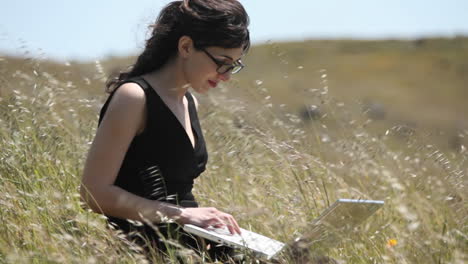 A-woman-using-a-laptop-sits-in-a-field-1