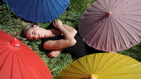 A-woman-lays-on-her-back-in-a-grassy-field-surrounded-my-different-colored-umbrellas