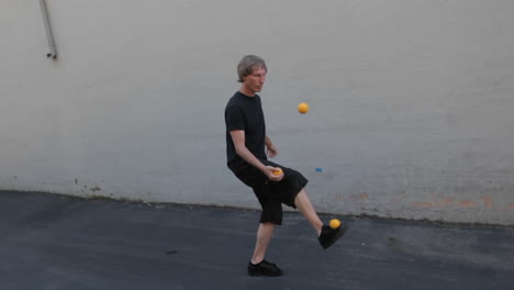 A-man-juggles-three-orange-balls-using-his-hands-and-feet