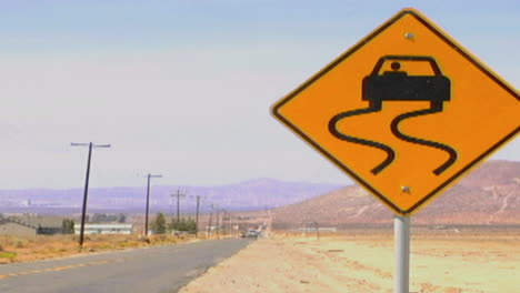 Cars-pass-by-a-slippery-when-wet-road-sign-along-a-lonely-desert-highway
