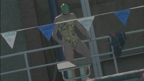 A-young-woman-stretches-stands-up-on-the-platform-dives-into-the-pool-and-starts-swimming