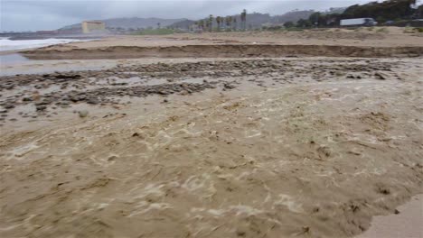 Panning-shot-of-Sanjon-Creek-washing-beach-sand-into-the-ocean-after-heavy-rain-in-Ventura-California