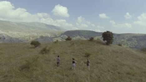 Antena-De-Drone-Sobre-Las-Tierras-Altas-De-La-Aldea-De-Lukomir-Y-Las-Montañas-De-Bosnia-Con-Tres-Personas-Corriendo-Por-Las-Laderas