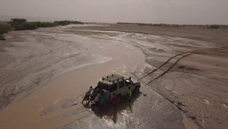 Aerial-Of-People-Pushing-A-4X4-Jeep-Out-Of-A-Muddy-River-In-The-Deserts-Of-Djibouti-Or-Somalia-Africa