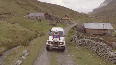 Luftaufnahme-Eines-Mannes-Mit-Helm,-Der-Auf-Der-Vorderseite-Eines-Jeeps-Durch-Ein-Dorf-Im-Kosovo-Fährt