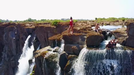 Antena-De-Un-Hombre-Y-Una-Mujer-Sentados-En-La-Cascada-De-La-Piscina-Del-Diablo-En-Victoria-Falls,-Zambia