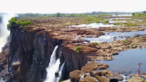 Antena-De-Un-Hombre-Y-Una-Mujer-Sentados-En-La-Cascada-De-Devil&#39;s-Pool-En-Victoria-Falls,-Zambia-1