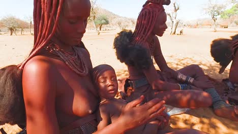 Himba-Stammesfrauen-Mit-Babys-Zeigen-Ihre-Schlammhaarverlängerungen-Und-Ungewöhnlichen-Geflochtenen-Dreadlock-Frisuren