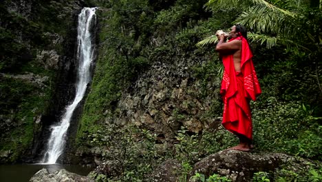A-Hawaii-native-performs-a-conch-ritual-in-front-of-a-tropical-waterfall