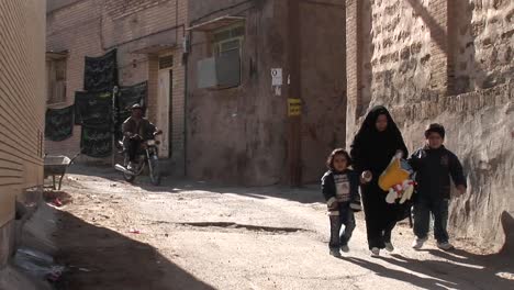 A-woman-wearing-a-chador-walks-with-two-children-down-an-ancient-alley-in-Iran-