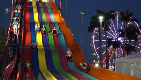 Children-ride-a-large-colorful-slide-next-to-a-Ferris-Wheel-at-night