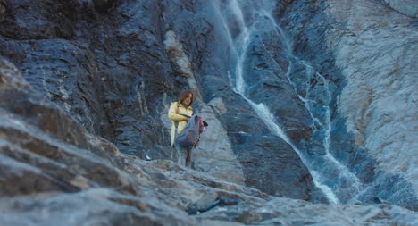 Hiker-Opens-Backpack-by-Waterfall