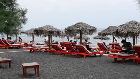 Greece-Santorini-Perissa-Tourists-Resting-On-Black-Sand-Beach