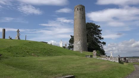 Irlanda-Clonmacnoise-Una-Torre-Redonda-Se-Eleva-Más-Allá-De-Una-Ladera-Cubierta-De-Hierba