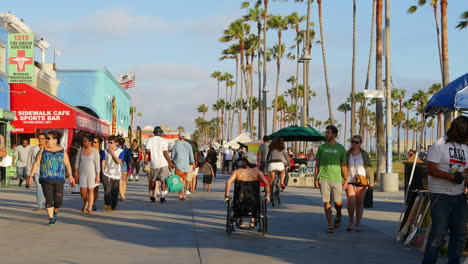 Los-Angeles-Venice-Beach-Boardwalk-Besucher-Gehen-An-Geschäften-Mit-Fahnen-Vorbei