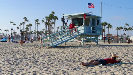 Los-Angeles-Venice-Beach-Rettungsschwimmer-Fegt-Turmrampe-Mit-Mann,-Der-Sich-Im-Vordergrund-Entspannt