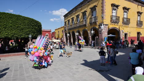 Mexico-San-Miguel-Balloon-Seller-And-Walking-Dog-In-A-Plaza