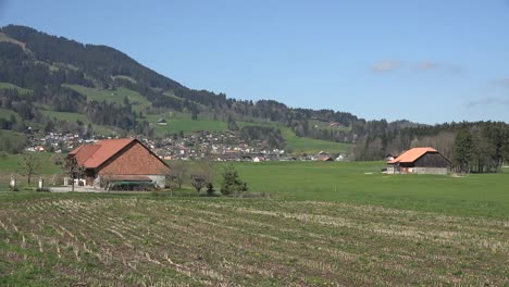 Switzerland-La-Gruyere-Farmhouses-And-Distant-Town-Zoom-In