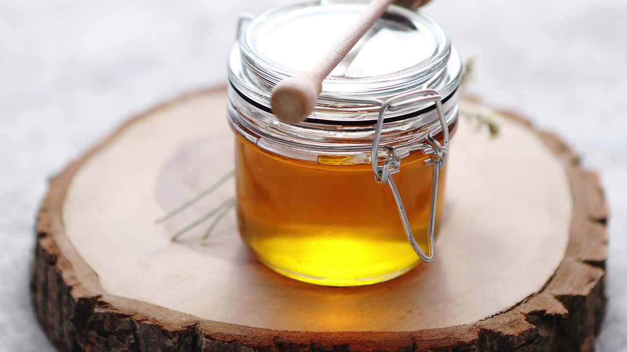 Premium stock video - Glass jar full of fresh honey placed on slice of wood