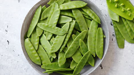 Fresh-green-peas-in-white-ceramic-bowl-on-gray-stone-background