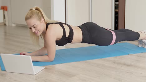 Blond-sexy-girl-doing-her-gym-workout-at-home-while-watching-online-video-lessons-on-laptop