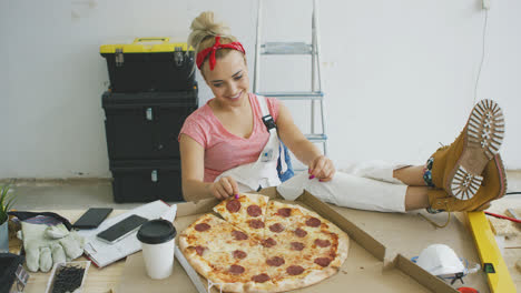 Woman-in-overalls-eating-pizza-at-workplace-