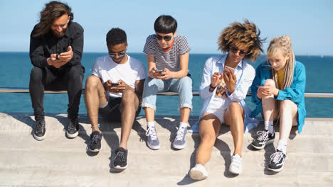 Young-diverse-people-with-mobile-phones-on-seafront-
