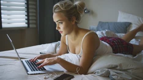 Woman-in-pajamas-using-laptop-on-bed