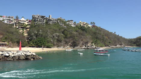 Mexico-Huatulco-boat-goes-by-view-of-boats-and-houses-on-hill